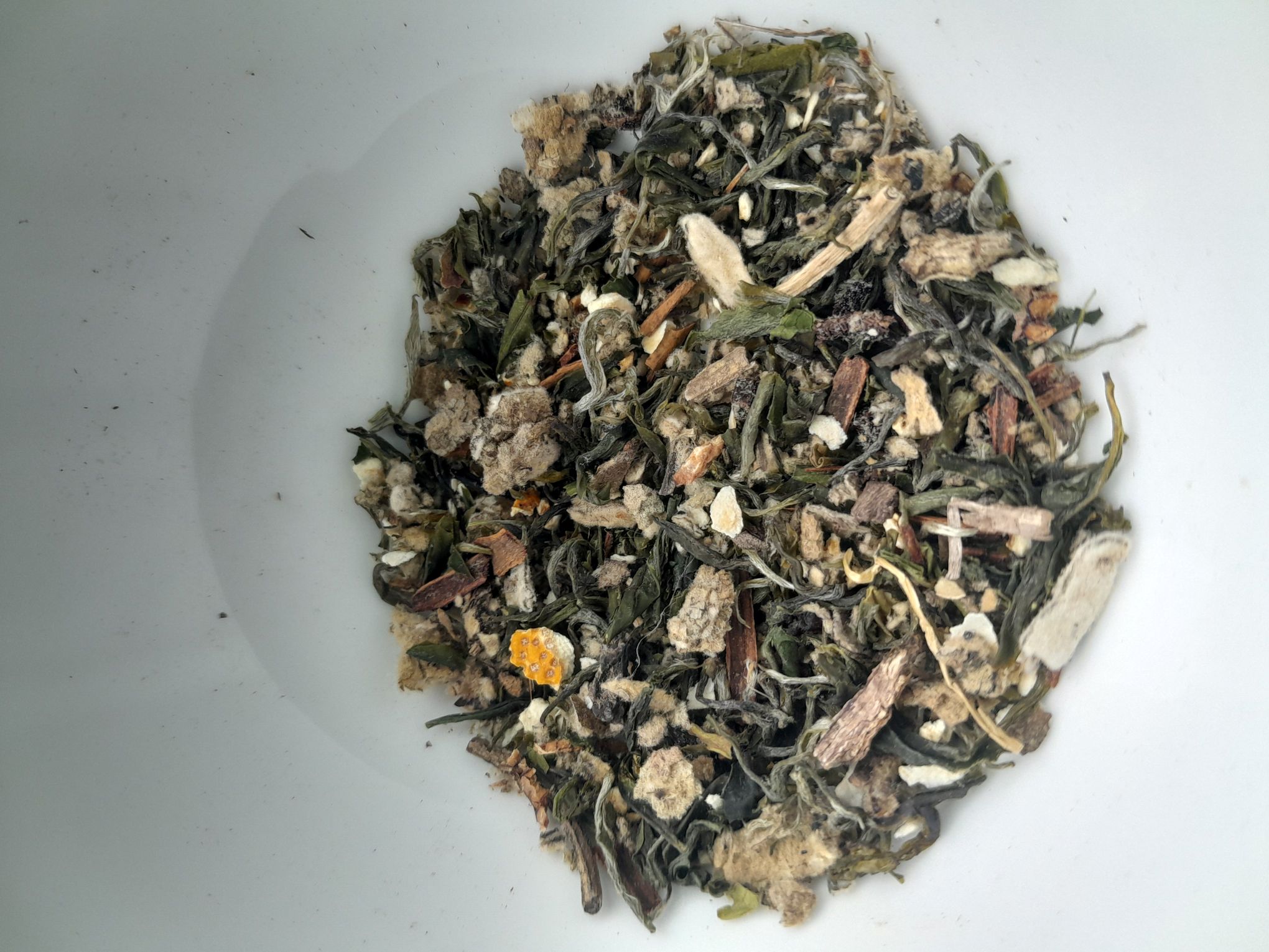 A loose-leaf tea blend full of shades of green and brown colors and containing green tea and other dried spices.